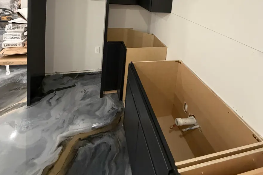 Open base cabinet showing plumbing rough-in above a poured metallic floor