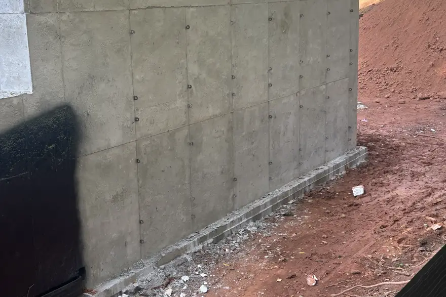 Poured concrete foundation wall standing against a red clay cut