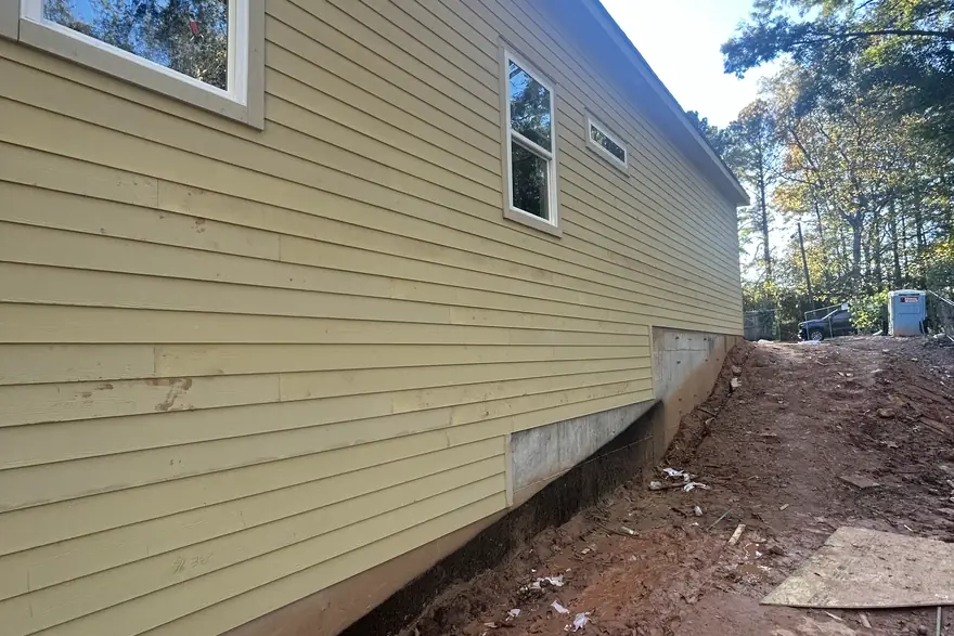 Lap siding and windows installed along the side of a home above a red clay bank