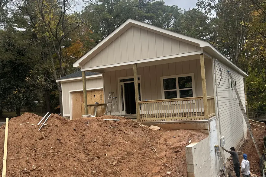 Crew grading and building a retaining wall around a nearly finished home on a cut clay bank